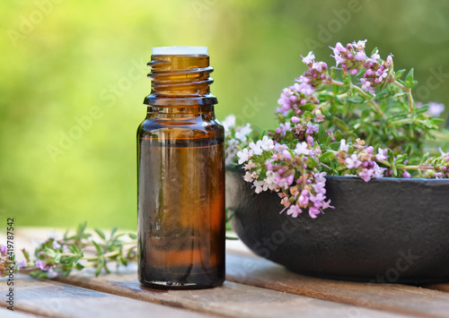 bottle of essential oil and lavender flowers on a table over green background