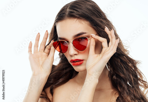 Brunette woman straightens glasses on her face and naked shoulders light background
