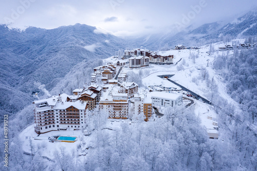 Winter aerial view of the Ski Resort Rosa Khutor and the mountain road to it. Beautiful winter landscape with frost-covered trees. Krasnaya Polyana, Sochi, Russia