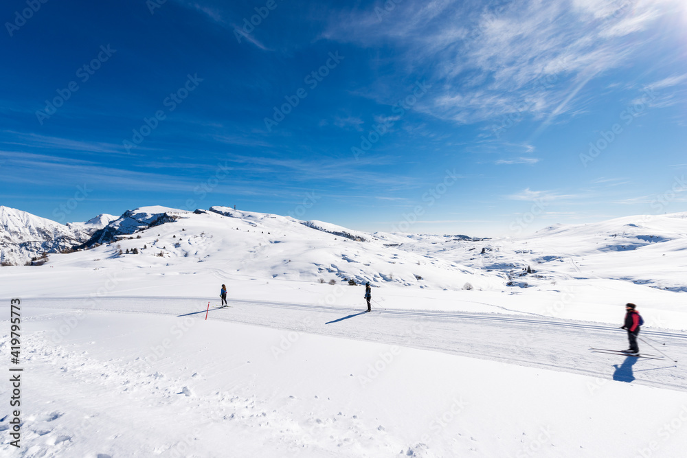 Three Cross-country Skiers on Lessinia Plateau, Malga San Giorgio ski resort. On background the snow capped peaks of Monte Carega or Small Dolomites. Bosco Chiesanuova, Verona, Veneto, Italy, Europe.