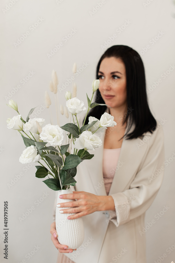 brunette girl in a light jacket holding a vase of flowers brunette girl in a light jacket holding a vase of flowers
