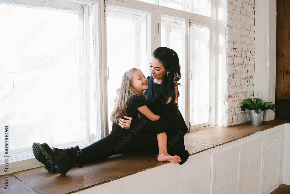 mom in black pantyhose and daughter with bare feet cuddle on the windowsill mom in black pantyhose and daughter with bare feet cuddle on the windowsill