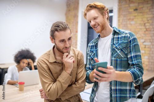Two male colleagues discussing something while looking at the phone abd looking enjoyed