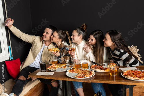 groups of young people take a selfie photo while eating pizzas at a restaurant