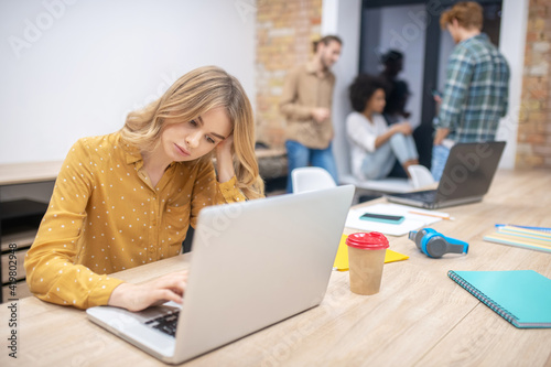 Blonde girl sitting at the laptop and looking bored and tired