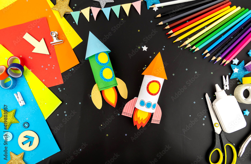 Two space rockets made of colored paper on a black table with colored ...