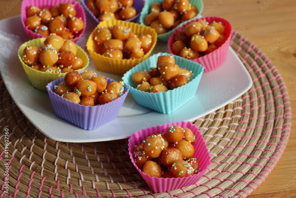 Traditional italian fried Struffoli with honey and sugar sprinkles on a plate on wooden table Traditional italian fried Struffoli with honey and sugar sprinkles on a plate on wooden table