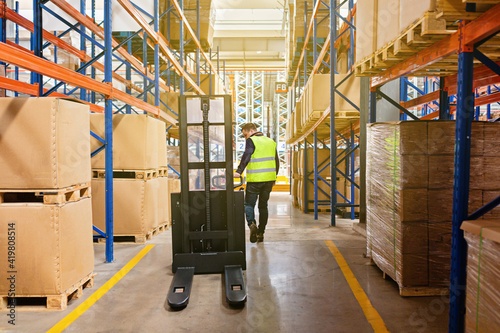 Storehouse employee in uniform working on forklift in modern automatic warehouse. Boxes are on the shelves of the warehouse. Warehousing, machinery concept. Logistics in stock.