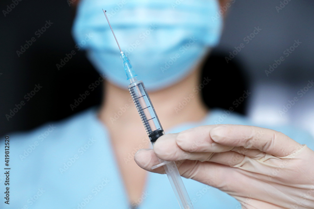 Nurse with syringe, woman in medical mask and protective gloves preparing to injection. Concept of vaccination during covid-19 pandemic	