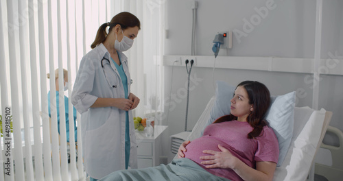 Fotografie Doctor wearing protective mask consulting pregnant woman resting in hospital bed