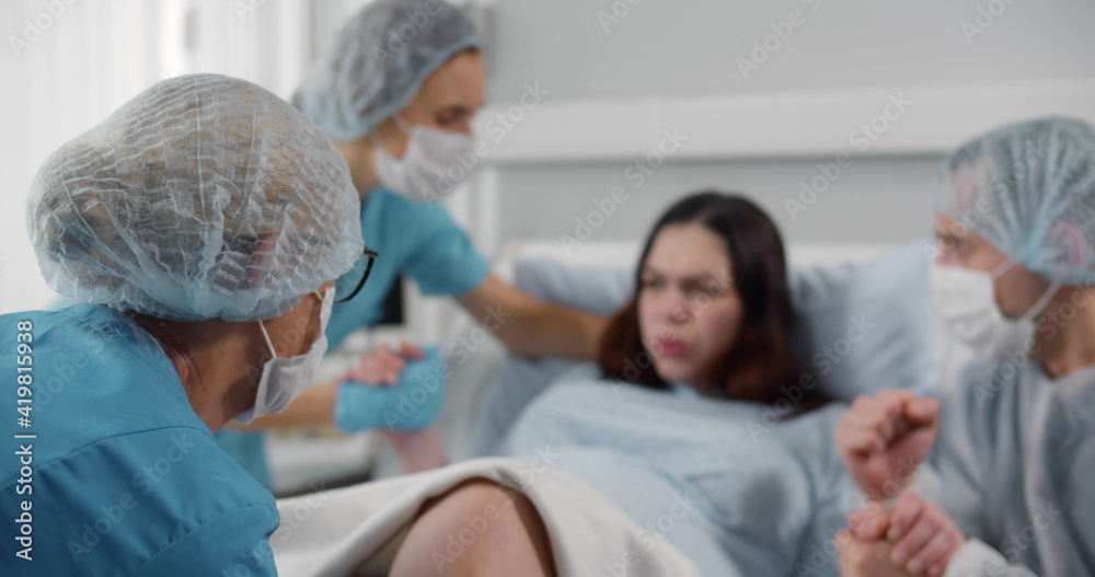 Obraz premium Pregnant woman in hospital giving birth with husband in mask holding her hand