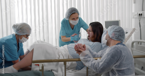 Photography Obstetricians and husband supporting female giving birth in hospital
