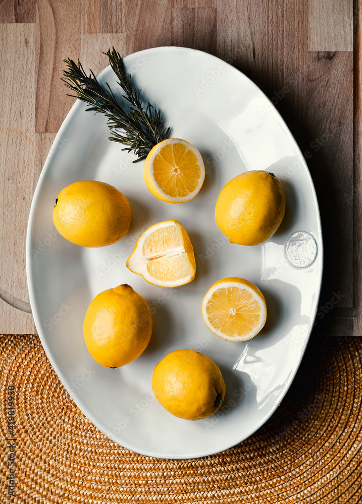 Lemons whole and cut in half, on a white plate, on wooden background Lemons whole and cut in half, on a white plate, on wooden background