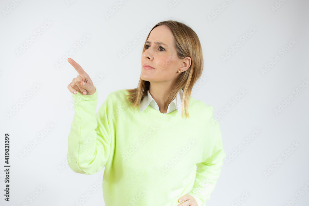 Excited young woman with casual sweater is looking away and trying to touch something with index finger. Waist up studio shot on white background. Excited young woman with casual sweater is looking away and trying to touch something with index finger. Waist up studio shot on white background.