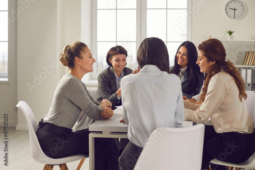 Team of women planning new project and choosing business strategy together. Group of positive businesswomen in their 20s and 30s meeting around office table, sharing opinions and discussing ideas photo
