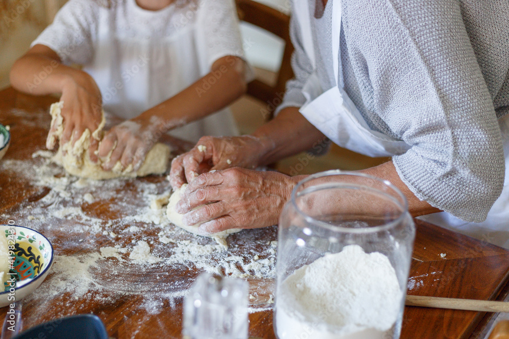 Frame image of the hands of an old woman and a child kneading dough, top view of the dough.
