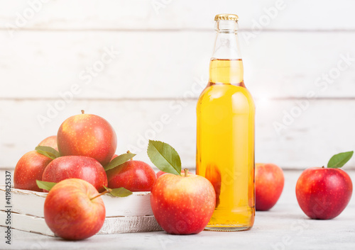 Bottle of homemade organic apple cider with fresh apples in box on wooden background with sun light