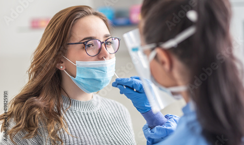 Female patient wearing mask over mouth is having sample taken from nose for a pcr test for Covid 19 photo