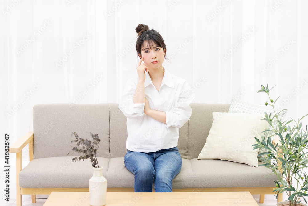 窓際のソファに座って考え事をする若い女性