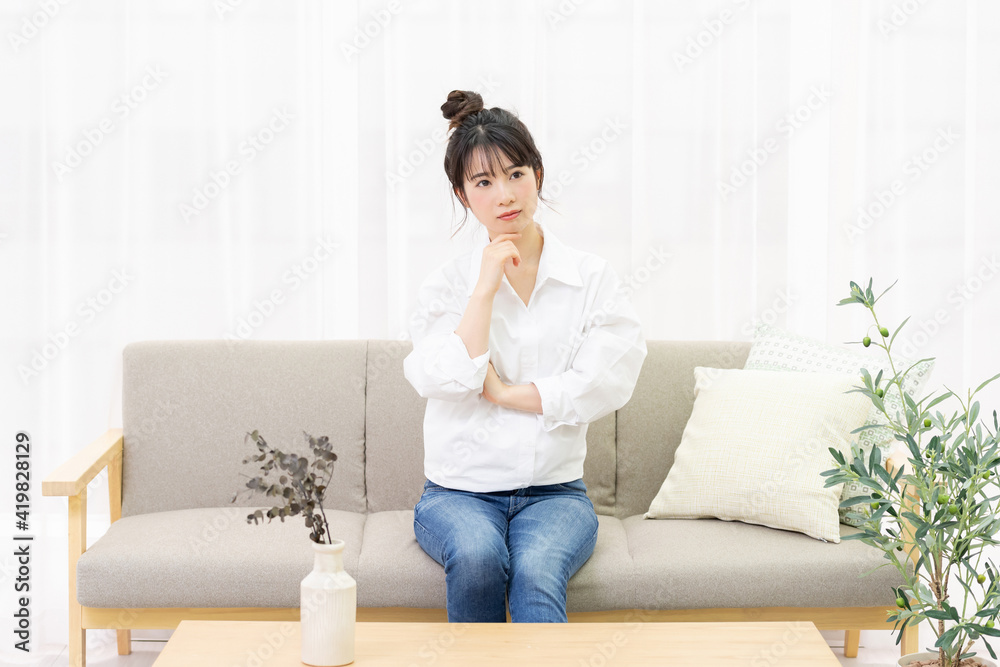 窓際のソファに座って考え事をする若い女性 窓際のソファに座って考え事をする若い女性