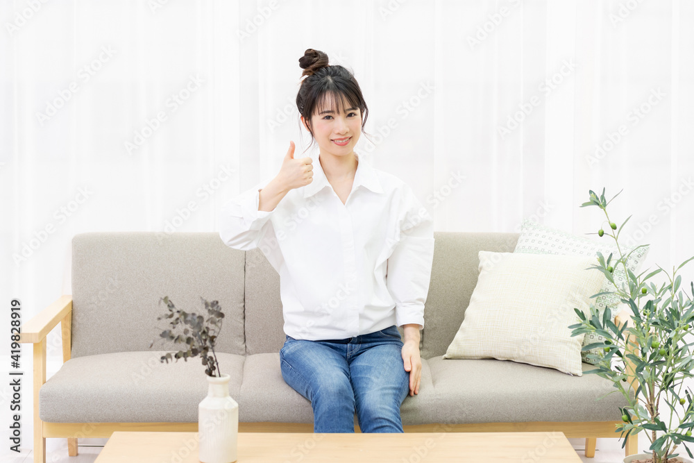 窓際のソファに座って、いいねのジェスチャーをする若い女性 窓際のソファに座って、いいねのジェスチャーをする若い女性
