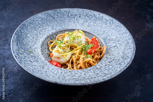 Modern design traditional fried scallops with tomatoes, broccoli pesto and Italian spaghetti pasta served as close-up on a Nordic design plate with copy space