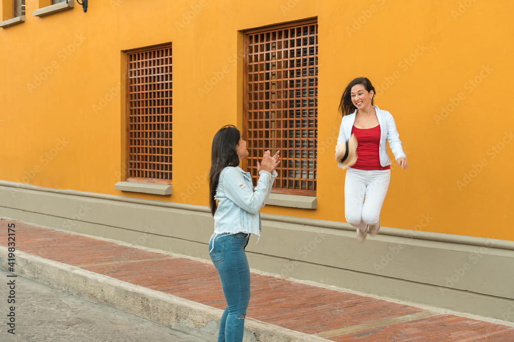 Enthusiastic woman jumping in the street and looking at her friend