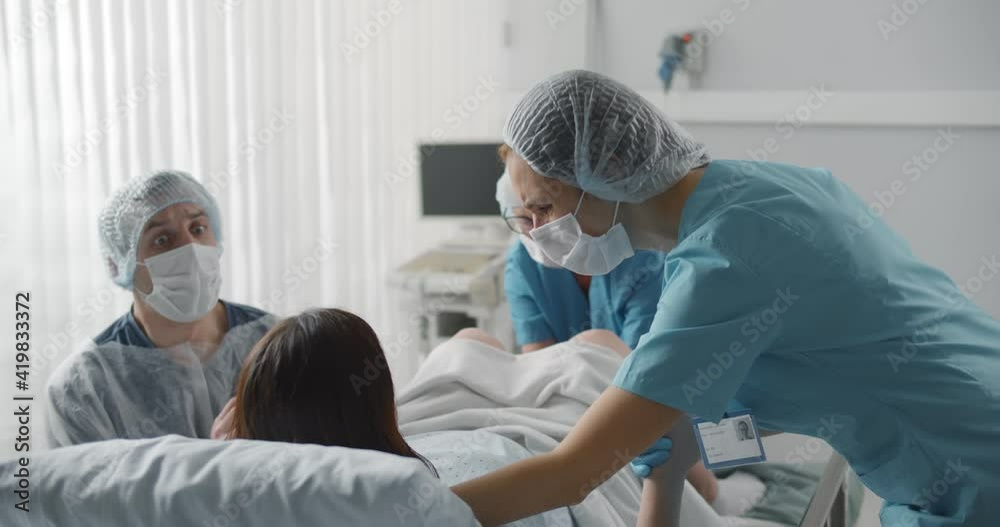 Woman giving birth with husband holds her hand in support and obstetricians assisting.