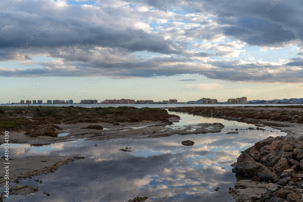 reflections of sky in rocky tidal pools with the hotels of La Manga del Mar Menor in the background