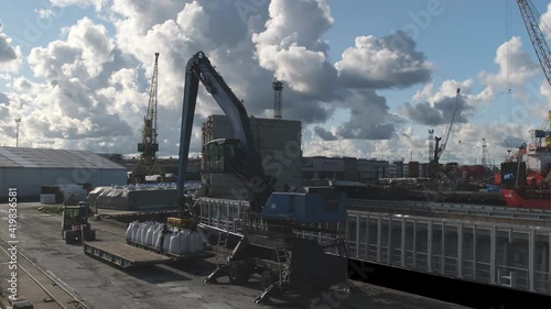large metal crane puts white bags with mineral fertilisers on steamboat deck in local harbour under cloudy sky timelapse