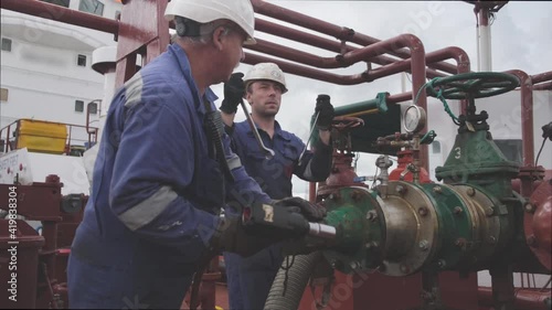 skilled engineers repair oil tanker pipeline of green and silver colours near large valve under white cloudy sky