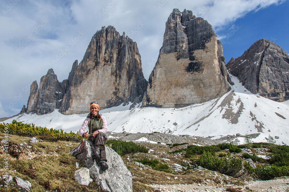 Young active woman sits on a stone in the dolomite alps overlooking the rocky peaks. Italy