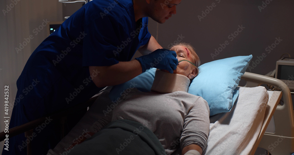 Nurse putting oxygen mask on elderly injured woman patient lying in hospital bed Nurse putting oxygen mask on elderly injured woman patient lying in hospital bed