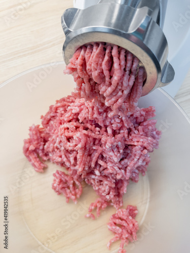 Meat grinder. Making homemade raw minced meat at kitchen. Close up of fatty pork minced.