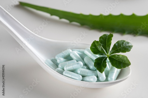 A spoon with a handful of capsules and a green leaf of aloe vera on white background. The concept of natural medicines. photo