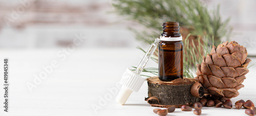 Banner, organic cosmetics concept, glass bottle with oil, pipette and cedar cone on light wooden background