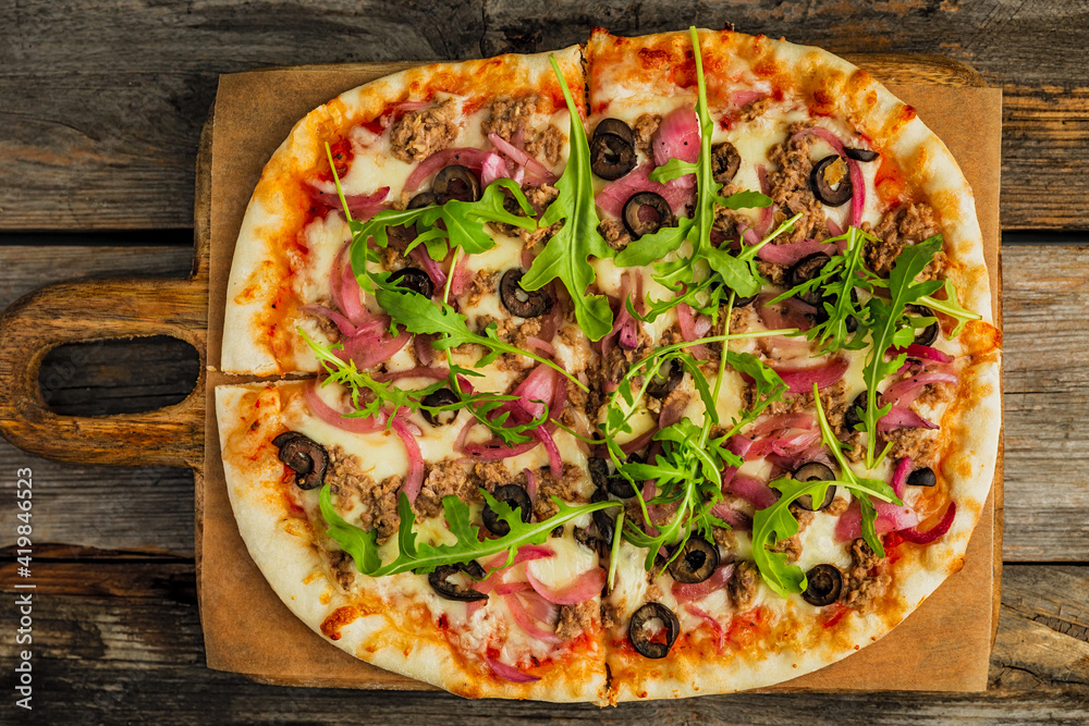 Pizza with minced meat, black olives, onion, rocket salad, cheese and tomato sauce, on wooden board, wooden rustic backdrop