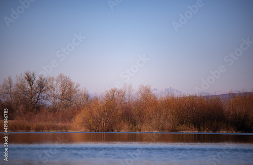 landscape with a huge lake at the end of the autumn season. rocky mountains and high forests on the distant horizon. silhouettes of leafless trees reflected in the luster of the water