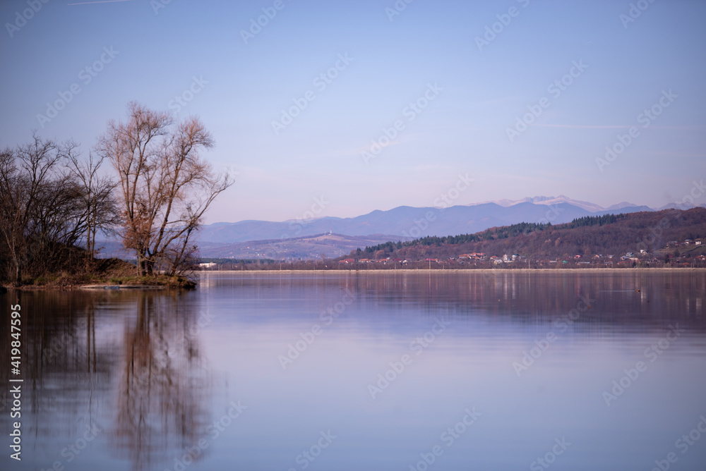landscape with a huge lake at the end of the autumn season. rocky mountains and high forests on the distant horizon. silhouettes of leafless trees reflected in the luster of the water