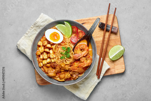 Laksa in gray bowl on concrete table top. Coconut noodle soup with chicken meat and prawns of peranakan cuisine. Asian food.