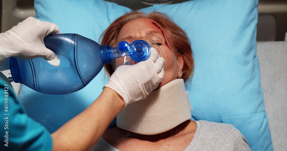Nurse in surgical gloves using bag valve mask giving oxygen to injured female patient in hospital Nurse in surgical gloves using bag valve mask giving oxygen to injured female patient in hospital