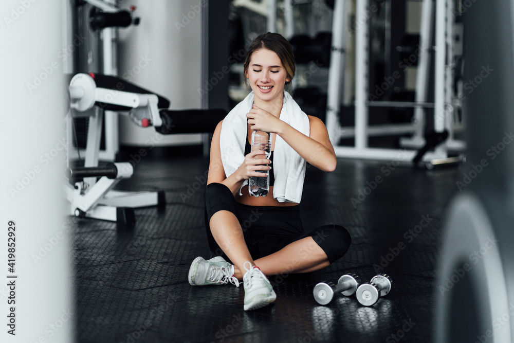 Attractive girl with a sports body on the floor in the gym drinks water, workout, lifestyle