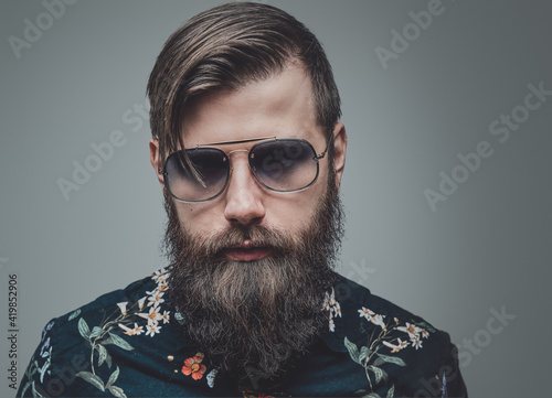 Fashionable man with sunglasses looking at camera in gray background. Closeup photography of a handsome and brutal hipster.