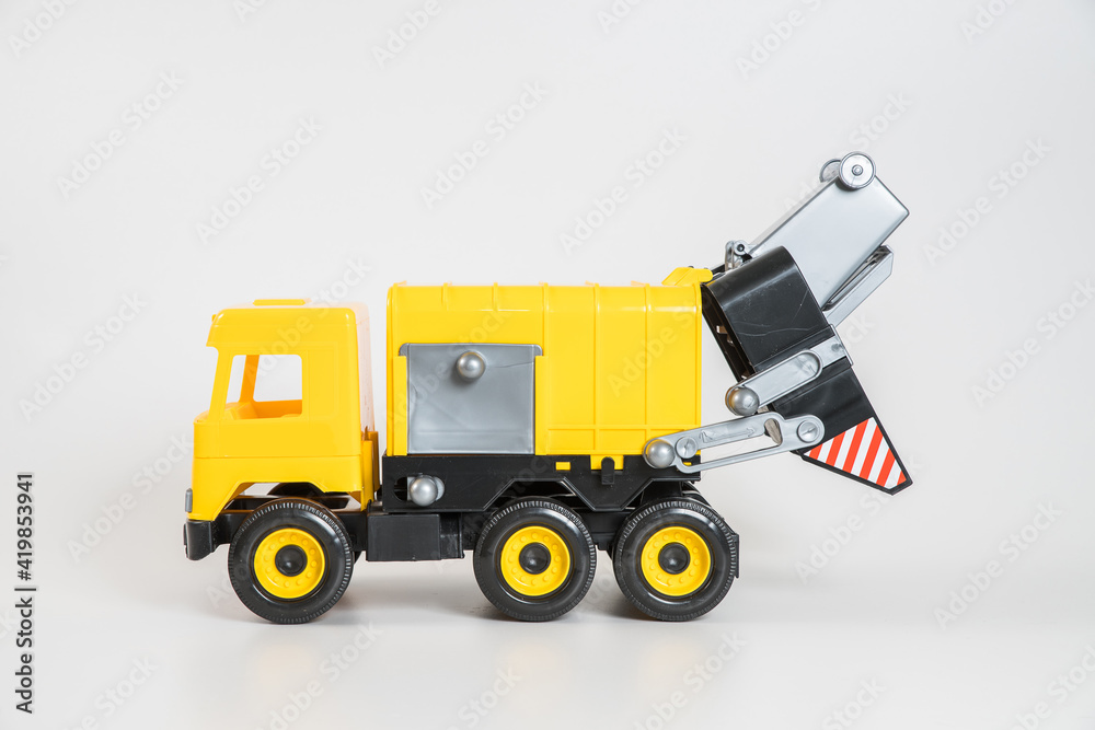 Plastic car. Toy model isolated on a white background. Yellow truck for the transport of garbage. Plastic car. Toy model isolated on a white background. Yellow truck for the transport of garbage.