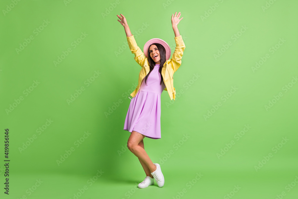 Photo of pretty lady raise hands dance wear yellow jacket violet dress pink cap sneakers isolated green color background Photo of pretty lady raise hands dance wear yellow jacket violet dress pink cap sneakers isolated green color background