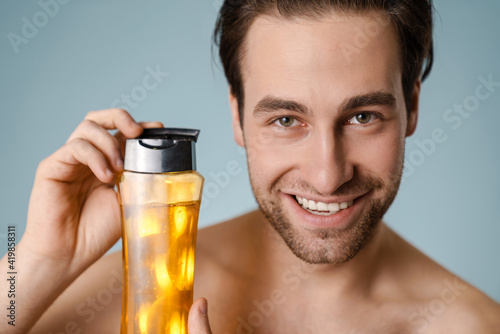 Close up of a smiling young nude man presenting shampoo