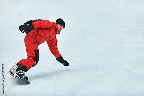 Male snowboarder in a red suit rides on the snowy hill with snowboard, Skiing and snowboarding concept