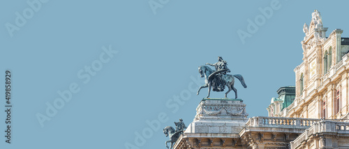 Banner with top roof sculpture of Greek goddess Muse riding Pegasus, a winged horse, at Vienna State Opera House, Vienna, Austria, with copy space. Concept of Cultural Heritage and Travel. photo