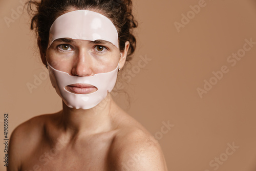 Half-naked woman looking at camera while posing in facial mask