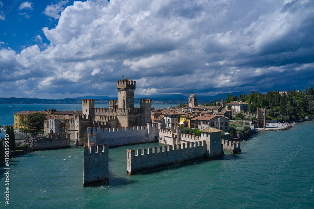 Rocca Scaligera Castle in Sirmione. Aerial view on Sirmione sul Garda. Italy, Lombardy. Cumulus clouds over the island of Sirmione. Aerial photography with drone.